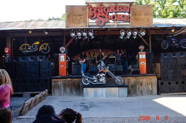 A band performing on the outdoor stage at The Broken Spoke Saloon in Sturgis, beneath a chopper motorcycle display