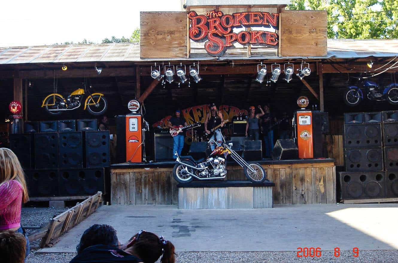 A band performing on the outdoor stage at The Broken Spoke Saloon in Sturgis, beneath a chopper motorcycle display