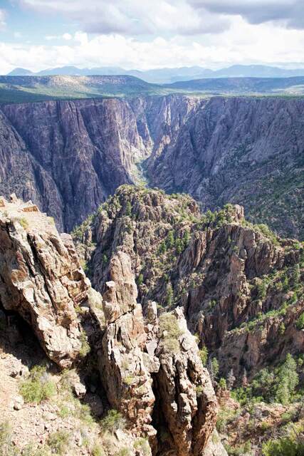 A dramatic view down the Black Canyon of the Gunnison, with sheer rock walls and distant mountains on the horizon