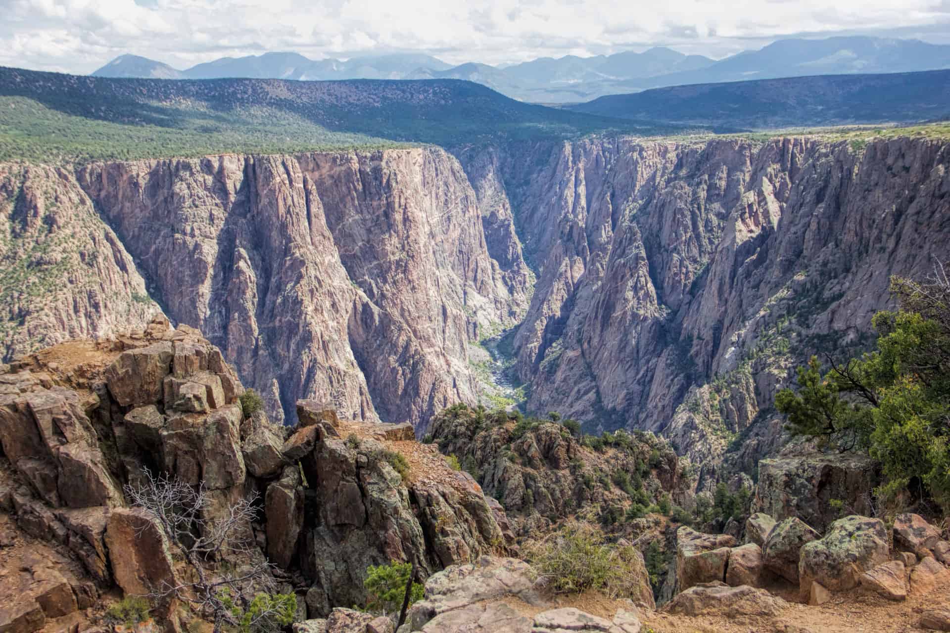 The dark, jagged walls of the Black Canyon of the Gunnison stretching toward distant mountains under a cloudy sky