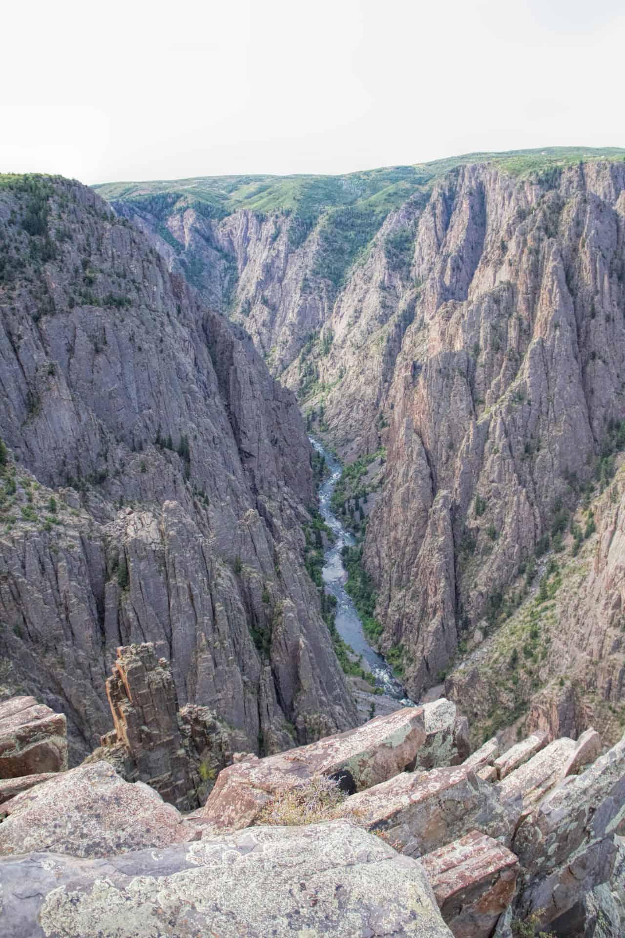 A narrow, steep view down into the Black Canyon of the Gunnison with the river cutting through the rock far below