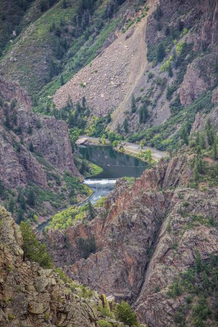 The Gunnison River curving past a small dam, roadway, and canyon walls dotted with autumn color