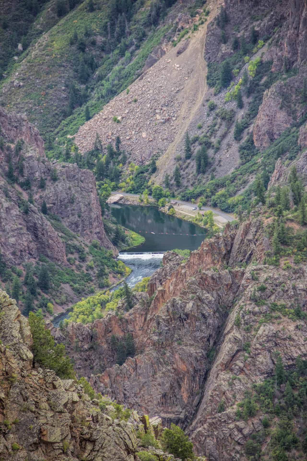 The Gunnison River curving past a small dam, roadway, and canyon walls dotted with autumn color