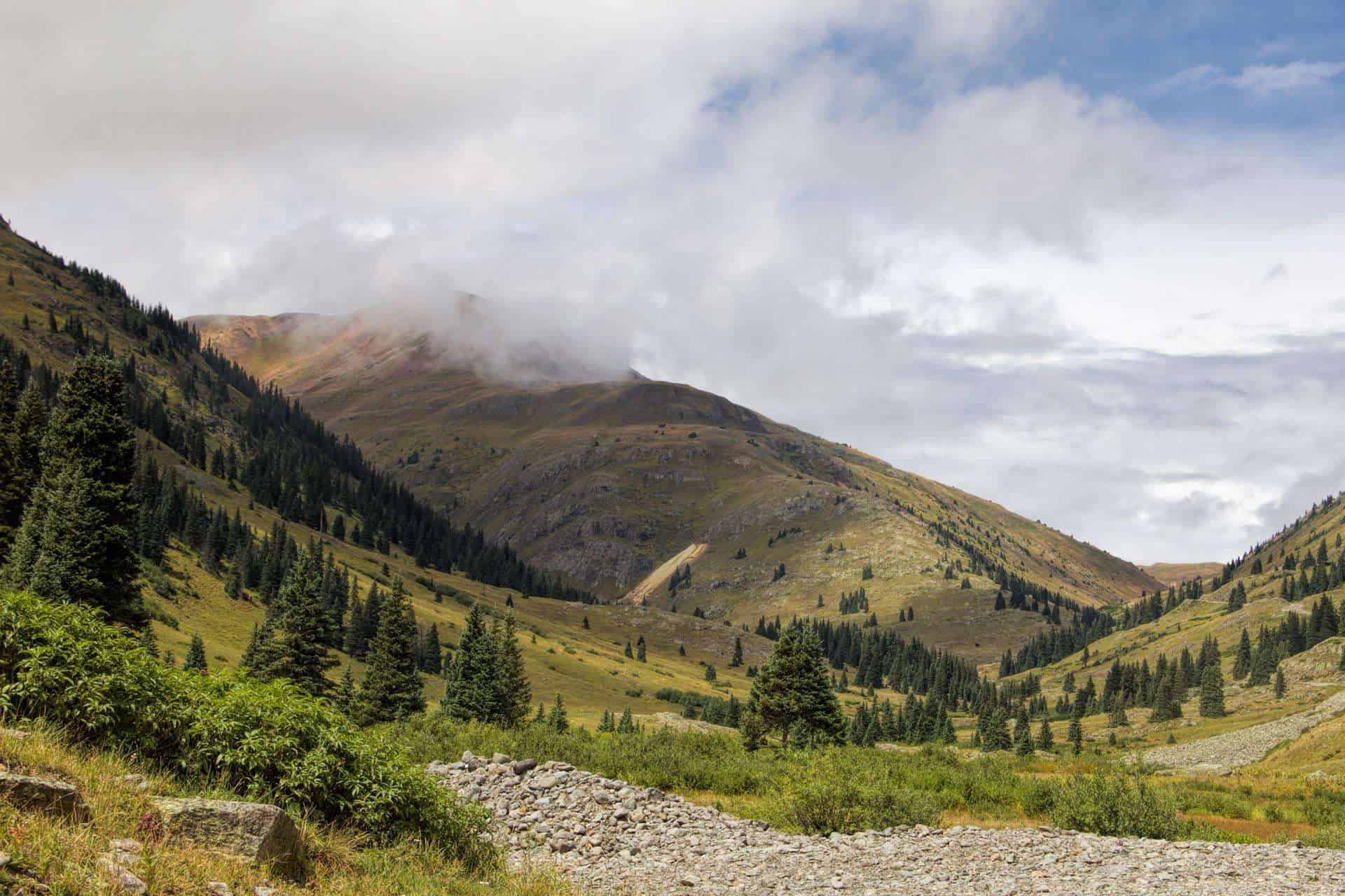 A high alpine valley with a dirt road winding toward a cloud-shrouded mountain peak