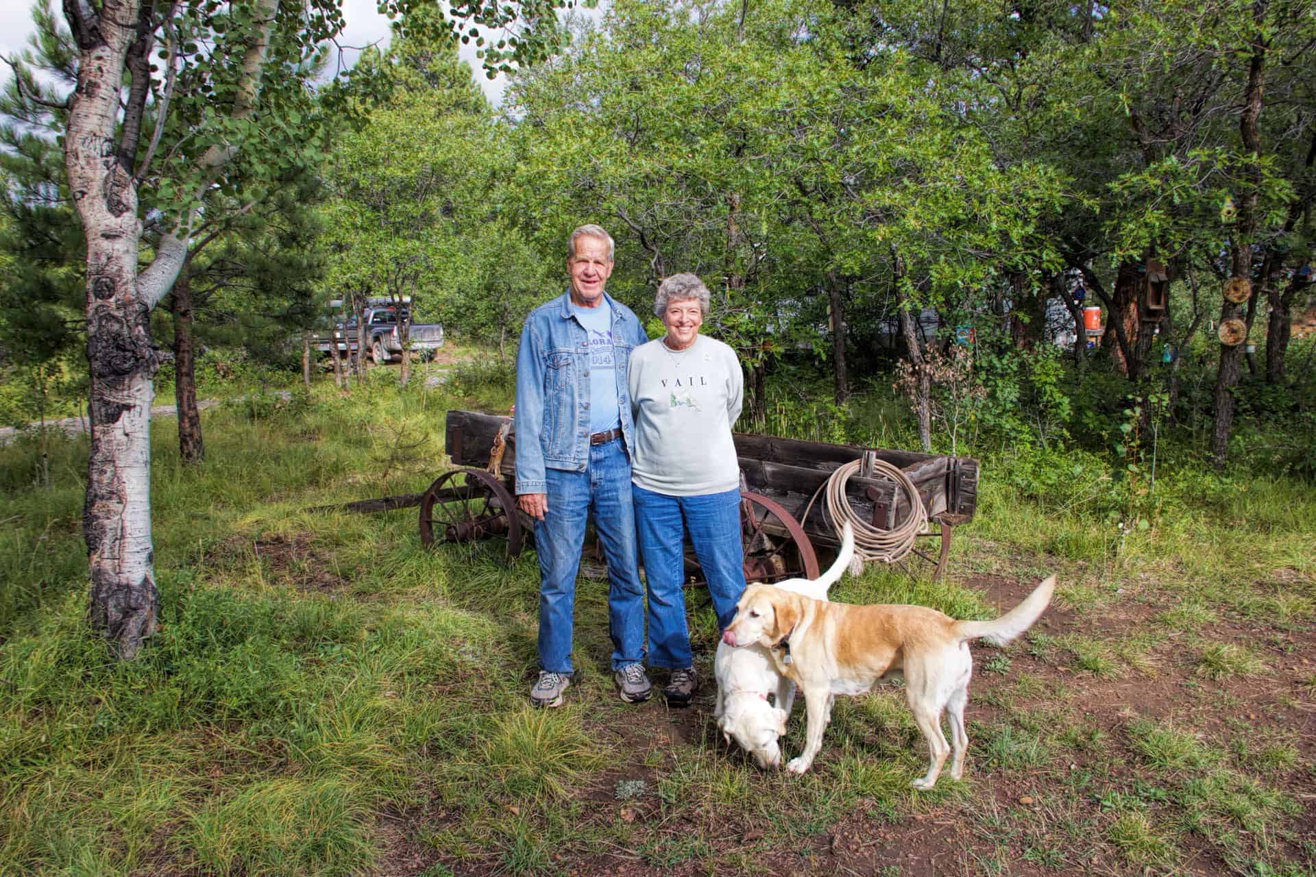 Larry and Marianne Williams standing beside an old wooden wagon with their two yellow labs, Mandy and Lacie