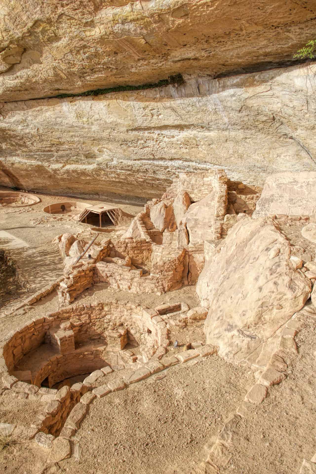 Ancestral Puebloan cliff dwelling ruins built into a sandstone alcove, with round kivas and stacked stone walls
