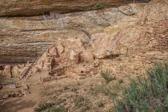 Stone masonry ruins of a cliff dwelling tucked beneath an overhanging sandstone cliff