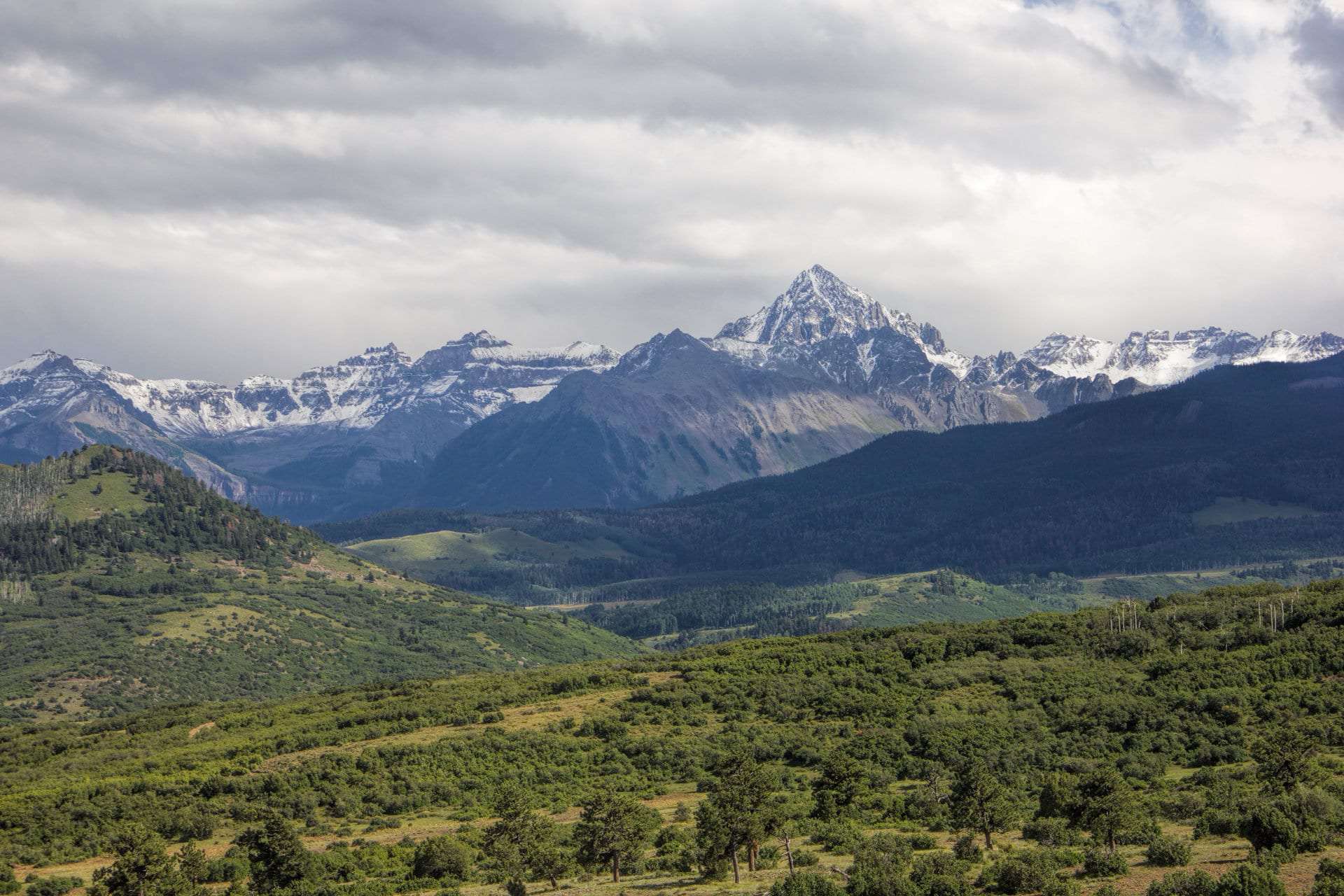 Snow-dusted peaks of the Sneffels Range towering above green foothills and forest