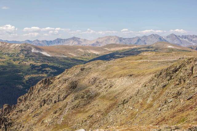 A sweeping view of mountain peaks and alpine tundra along Trail Ridge Road under a partly cloudy sky