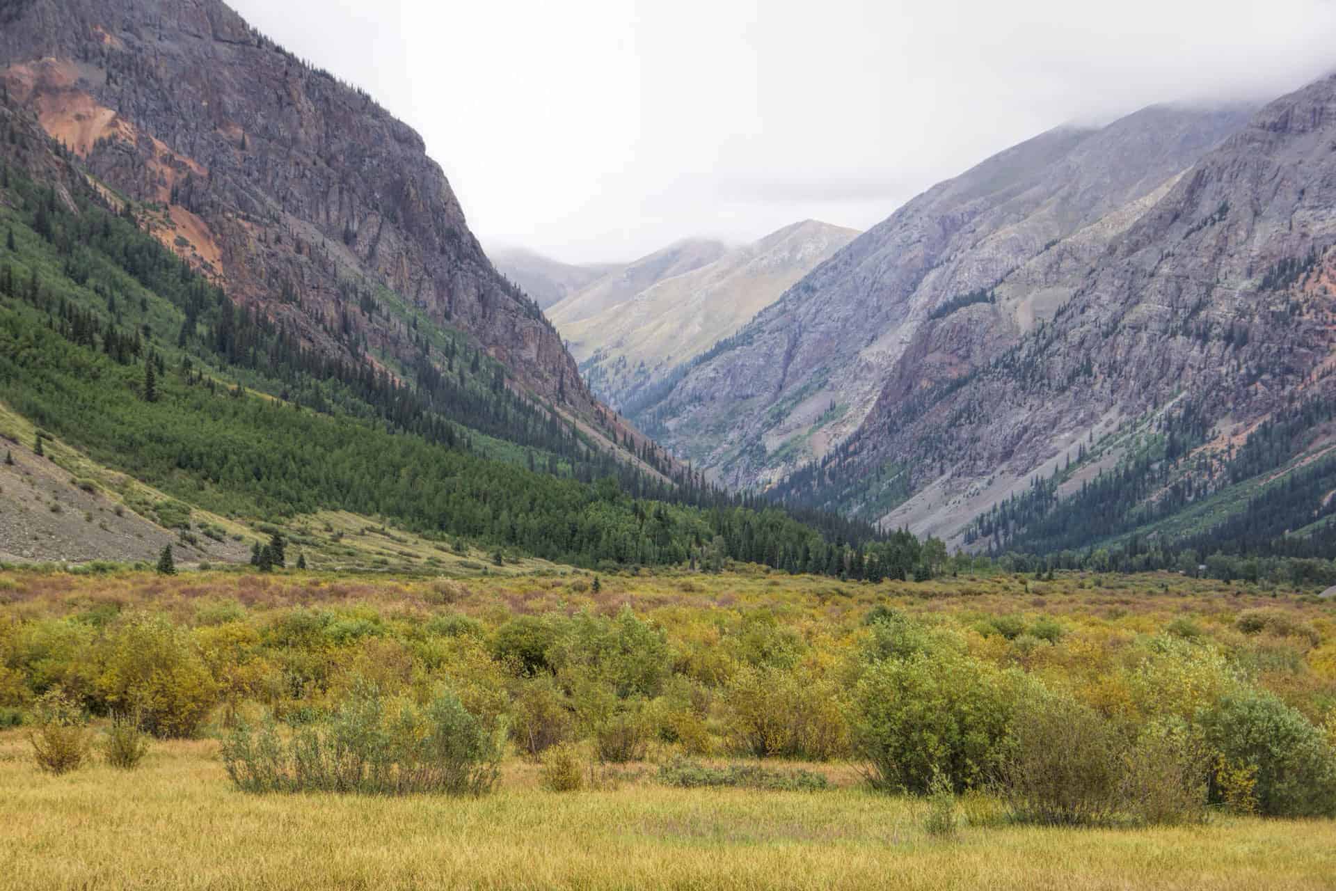 A rugged mountain valley with a winding rocky road leading between steep, snow-streaked peaks