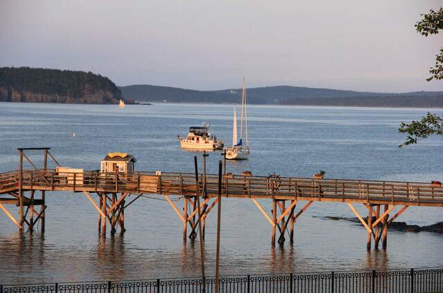 A wooden pier reaching into Frenchman Bay at Bar Harbor, with sailboats anchored offshore