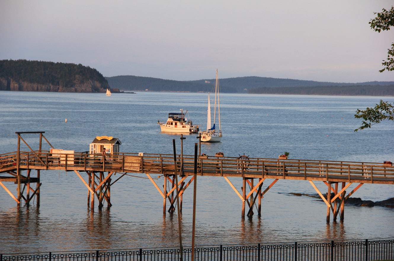 A wooden pier reaching into Frenchman Bay at Bar Harbor, with sailboats anchored offshore
