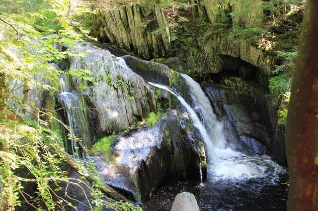 A waterfall cascading over layered rock in a forested gorge in Baxter State Park