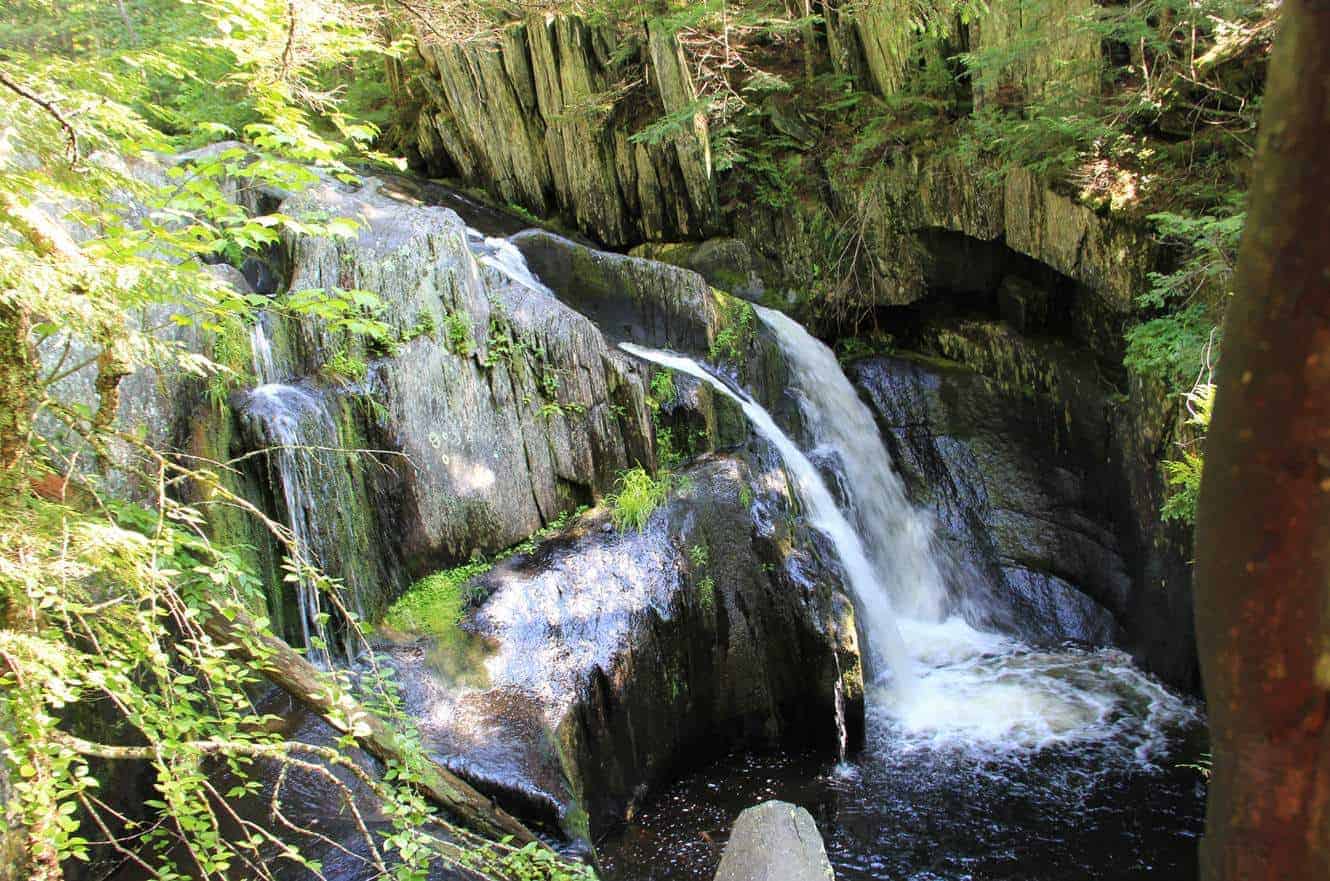 A waterfall cascading over layered rock in a forested gorge in Baxter State Park