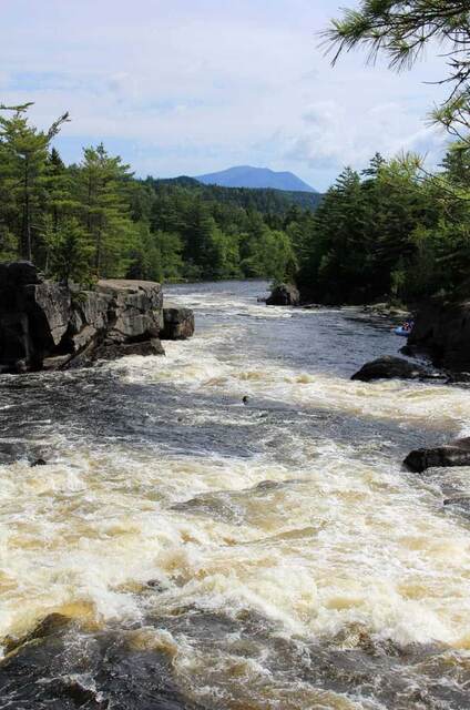 Whitewater rafters navigating the Penobscot River's class IV rapids, with Mount Katahdin in the background