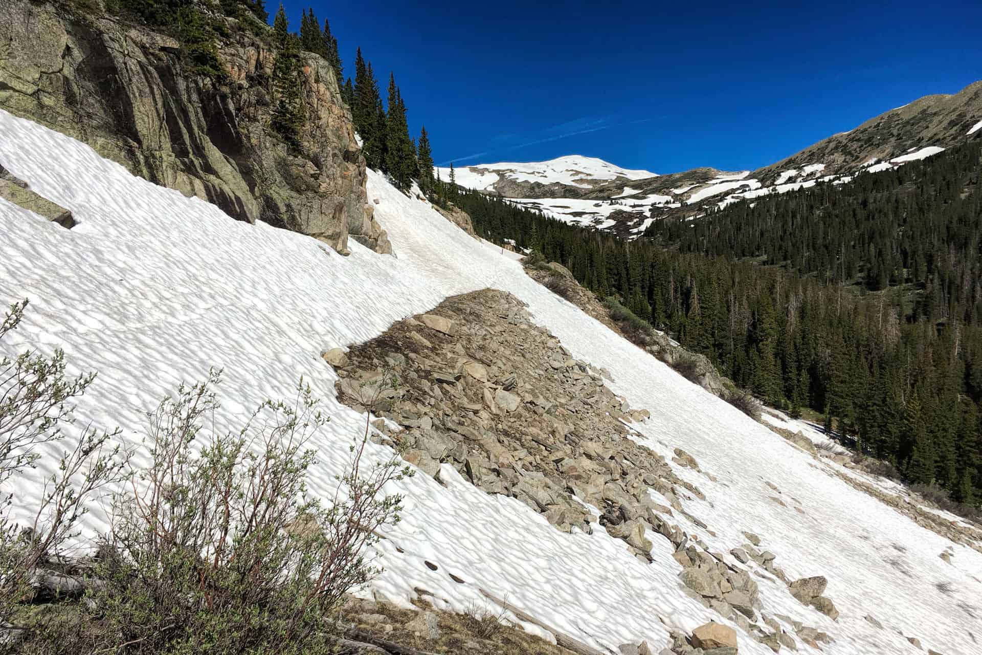 A steep, corrugated snowbank descending sharply between rock outcrops and pine trees