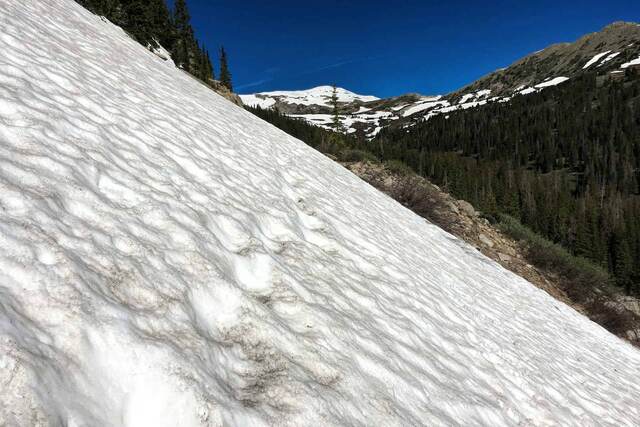 A close-up of a rippled snow slope with old footprints, framed by a distant snow-capped peak