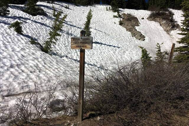 A weathered wooden trail sign reading 'Alpine Tunnel East Portal 1882-1910' standing before a wide snowfield