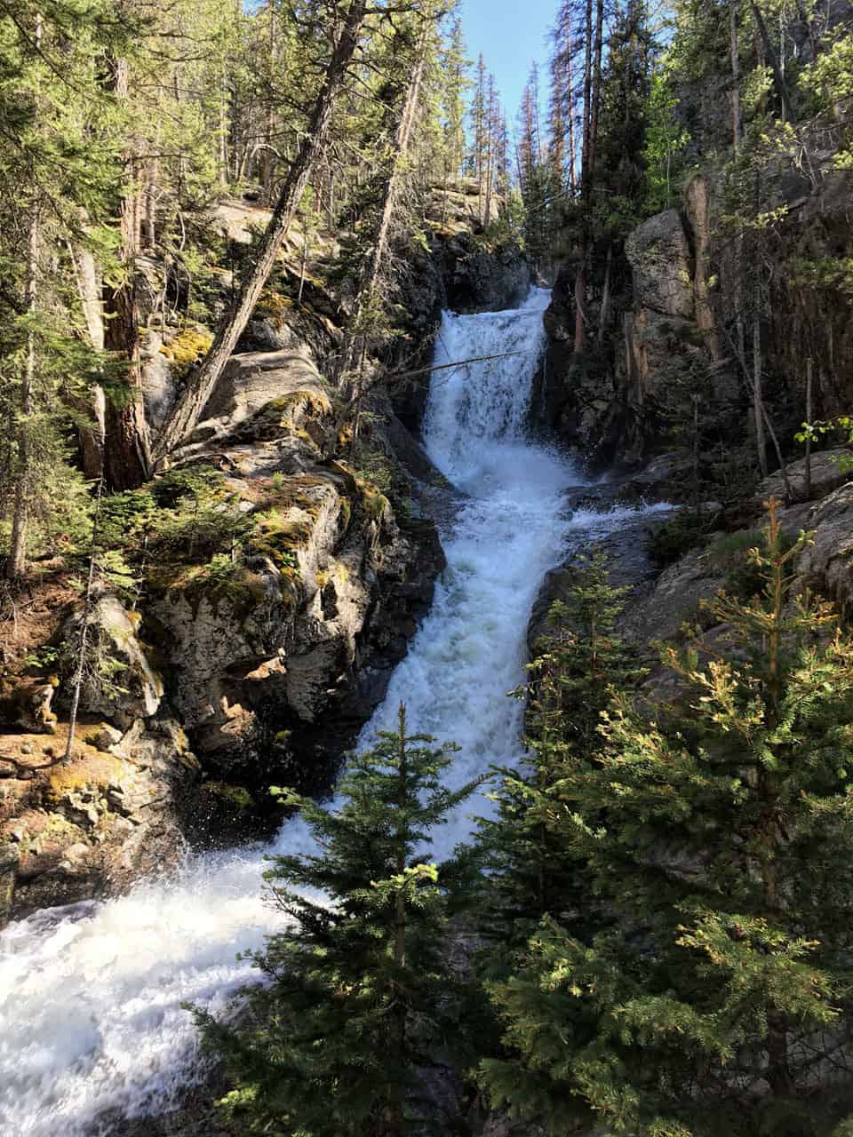 A tall, multi-tiered waterfall cascading through a narrow, forested rocky canyon