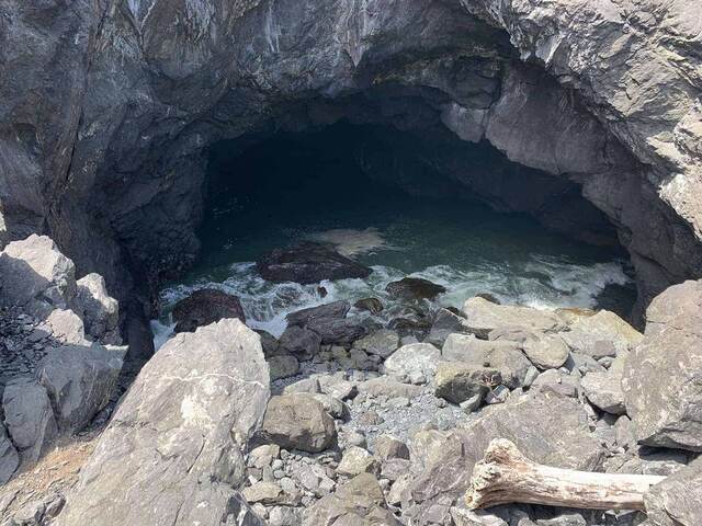 Looking into a sea cave at Sisters Rock, with dark water pooling inside and driftwood on the rocks below