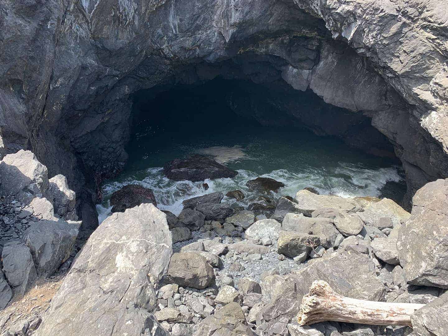 Looking into a sea cave at Sisters Rock, with dark water pooling inside and driftwood on the rocks below