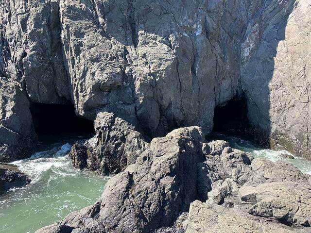 A closer view of two sea cave entrances in the cliff face, with waves washing between the rocks