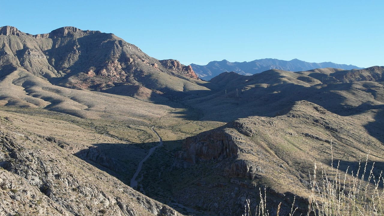 A mountain valley view with a dirt road winding through hazy blue-gray peaks