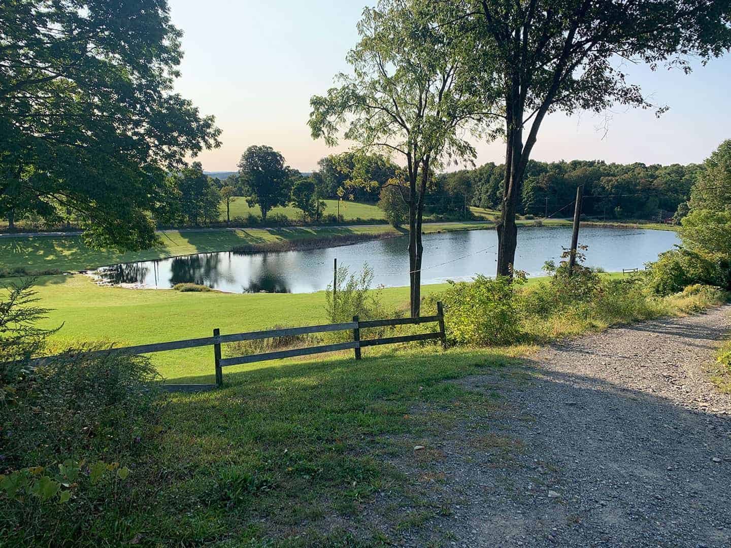 A quiet pond at sunset, seen past a wooden fence at Pleasant Acres Farm RV Resort
