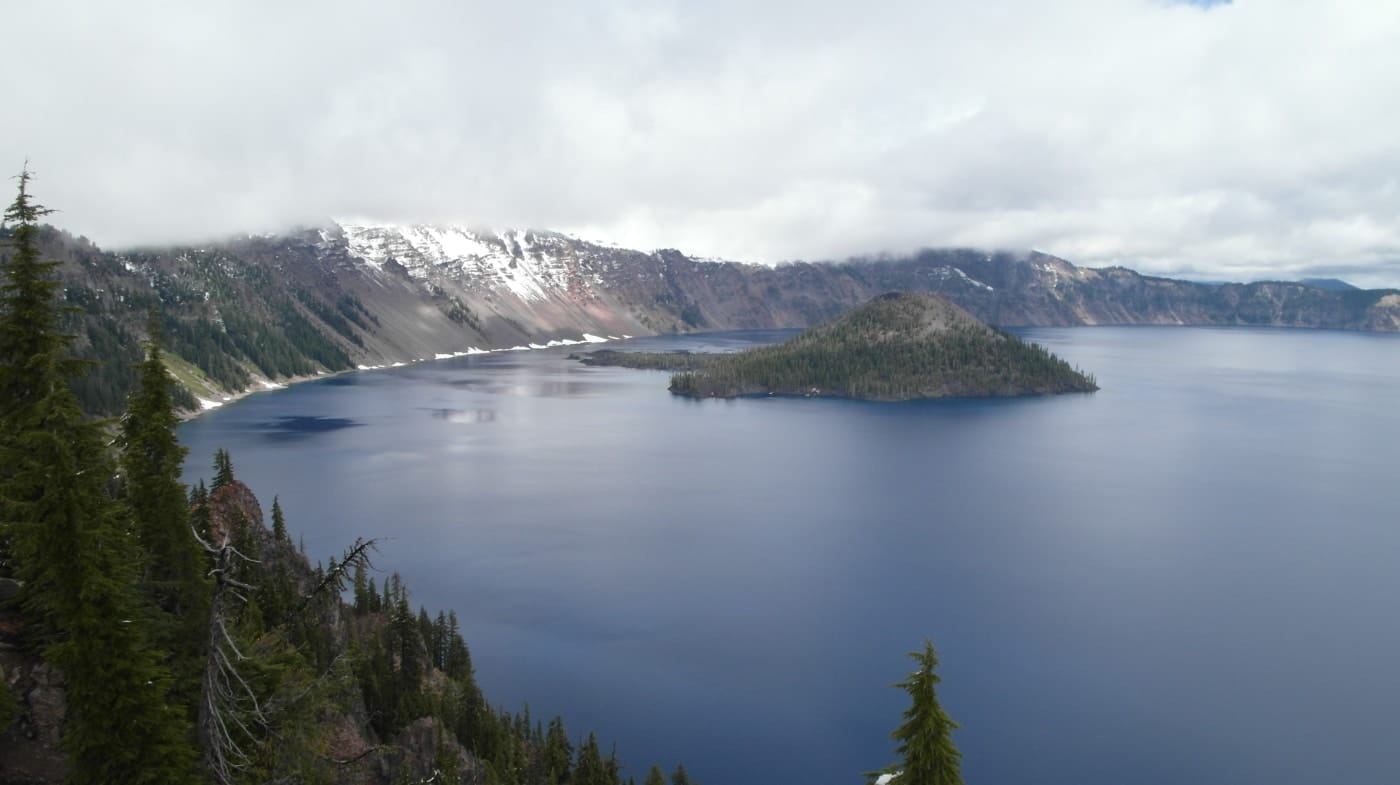Wizard Island rising from Crater Lake's brilliant blue water, with clouds reflected on the surface