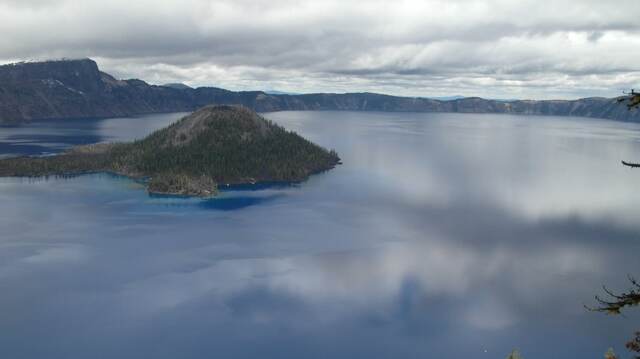 Crater Lake's rim and Wizard Island seen across the water under a partly cloudy sky