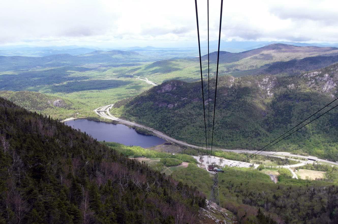 View from inside the tramway car looking down over Echo Lake and the highway winding through the notch, tram cables in the foreground