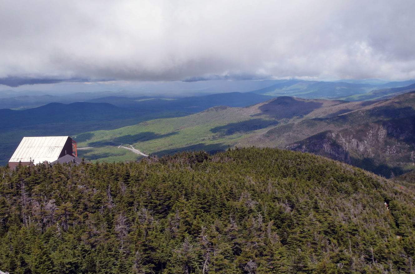 The summit observation building at Cannon Mountain, its boardwalk leading up through evergreens with layered mountains behind