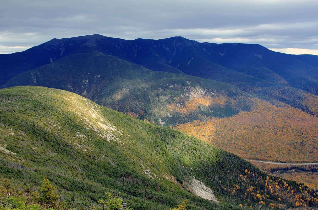 Fall foliage covering the slopes below the Franconia Ridge, orange and green patches against a darker forested ridgeline