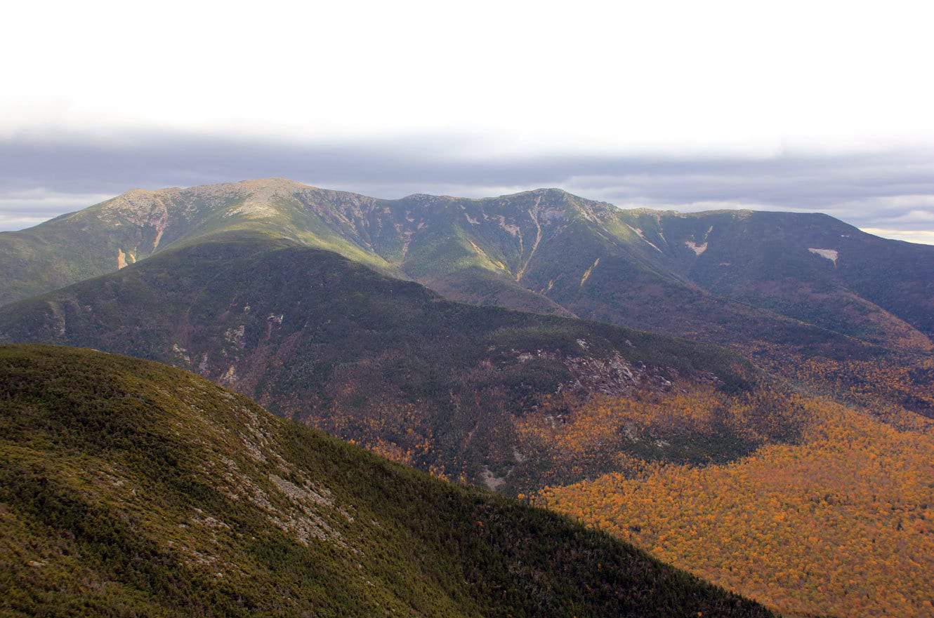 The bare rocky summits of the Franconia Ridge above fall-colored slopes and a forested foreground ridge