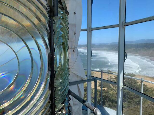 Close-up of the lighthouse's rotating Fresnel lens, with the Oregon coastline visible through the lantern room windows