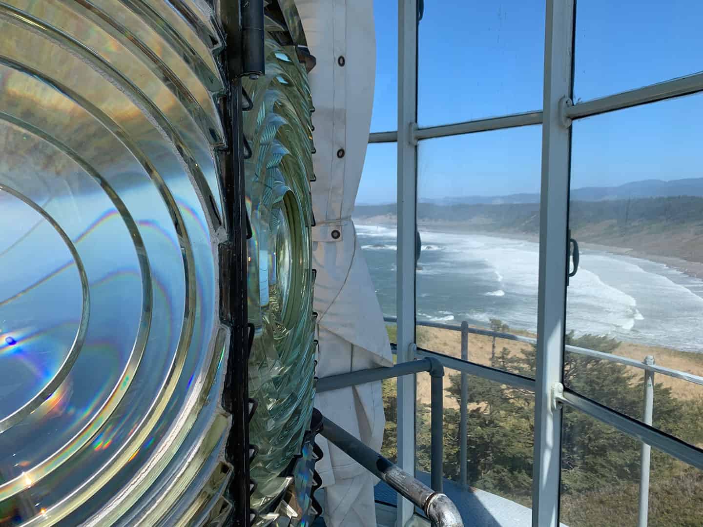 Close-up of the lighthouse's rotating Fresnel lens, with the Oregon coastline visible through the lantern room windows