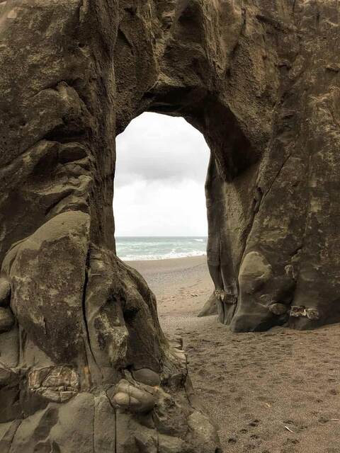 A natural rock archway framing a view of the sandy beach and ocean beyond