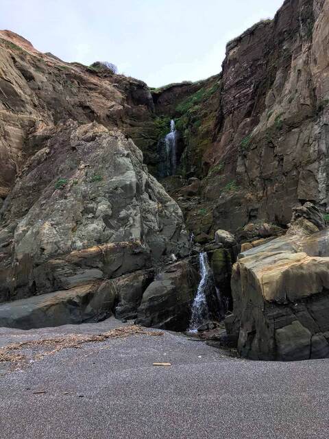 A pair of waterfalls cascading down a mossy rock cleft in the cliffside onto the beach below