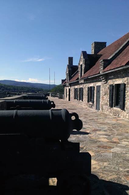 A row of black cannons along the ramparts walkway beside the stone barracks