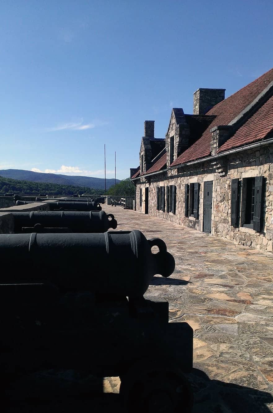 A row of black cannons along the ramparts walkway beside the stone barracks
