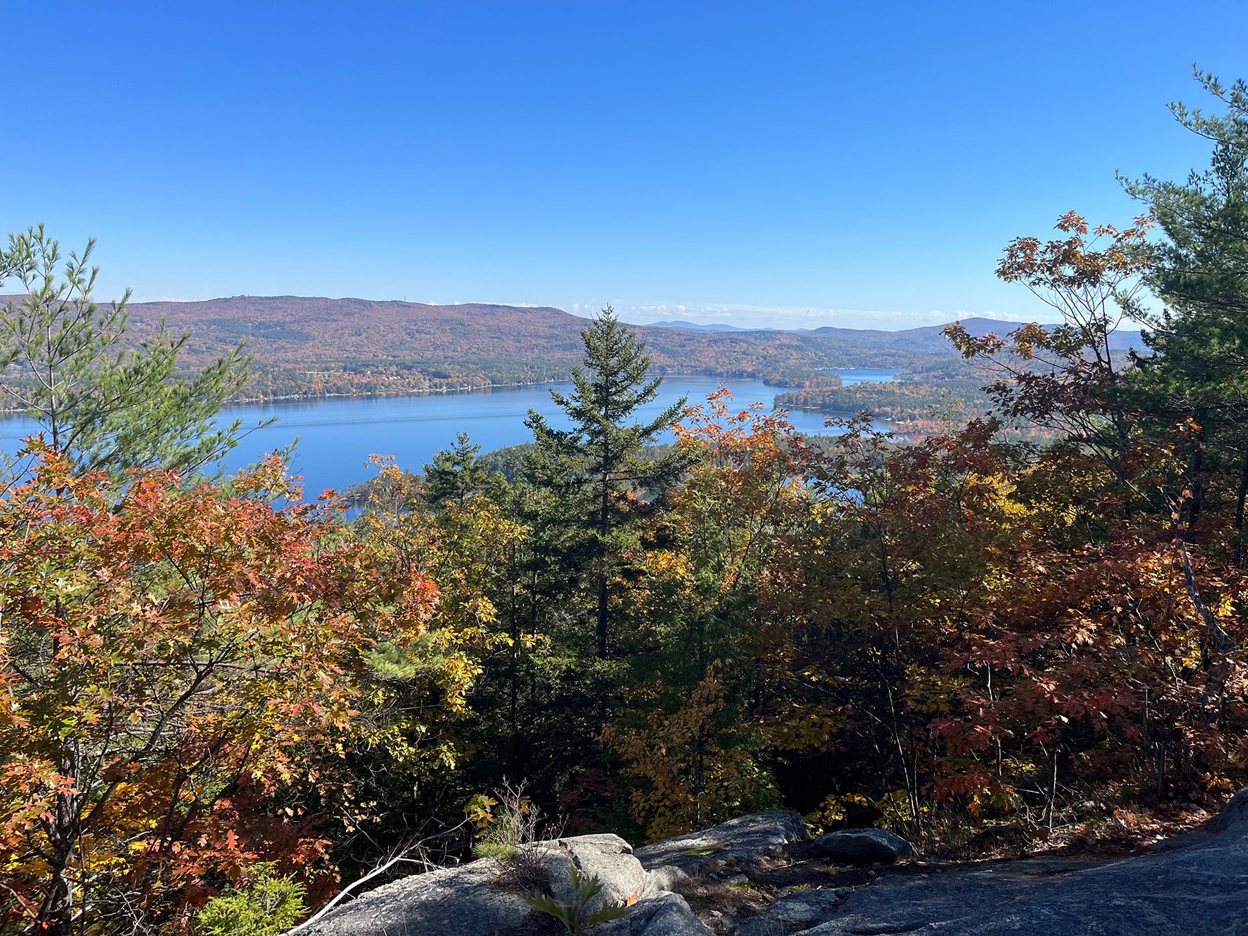 A wide lake winding between fall-colored shorelines, seen from a hillside overlook