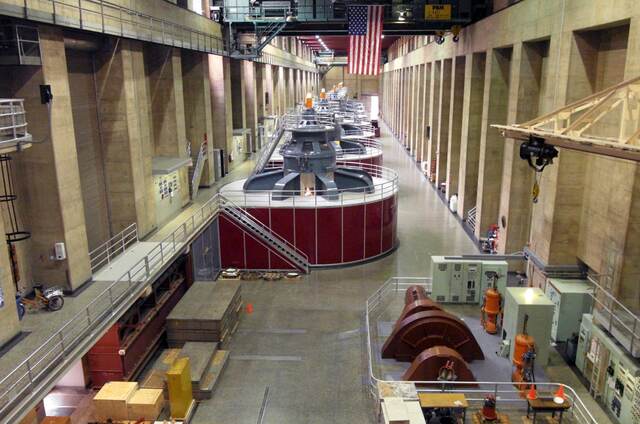 The generator hall inside Hoover Dam, its row of massive turbine housings lit beneath an American flag