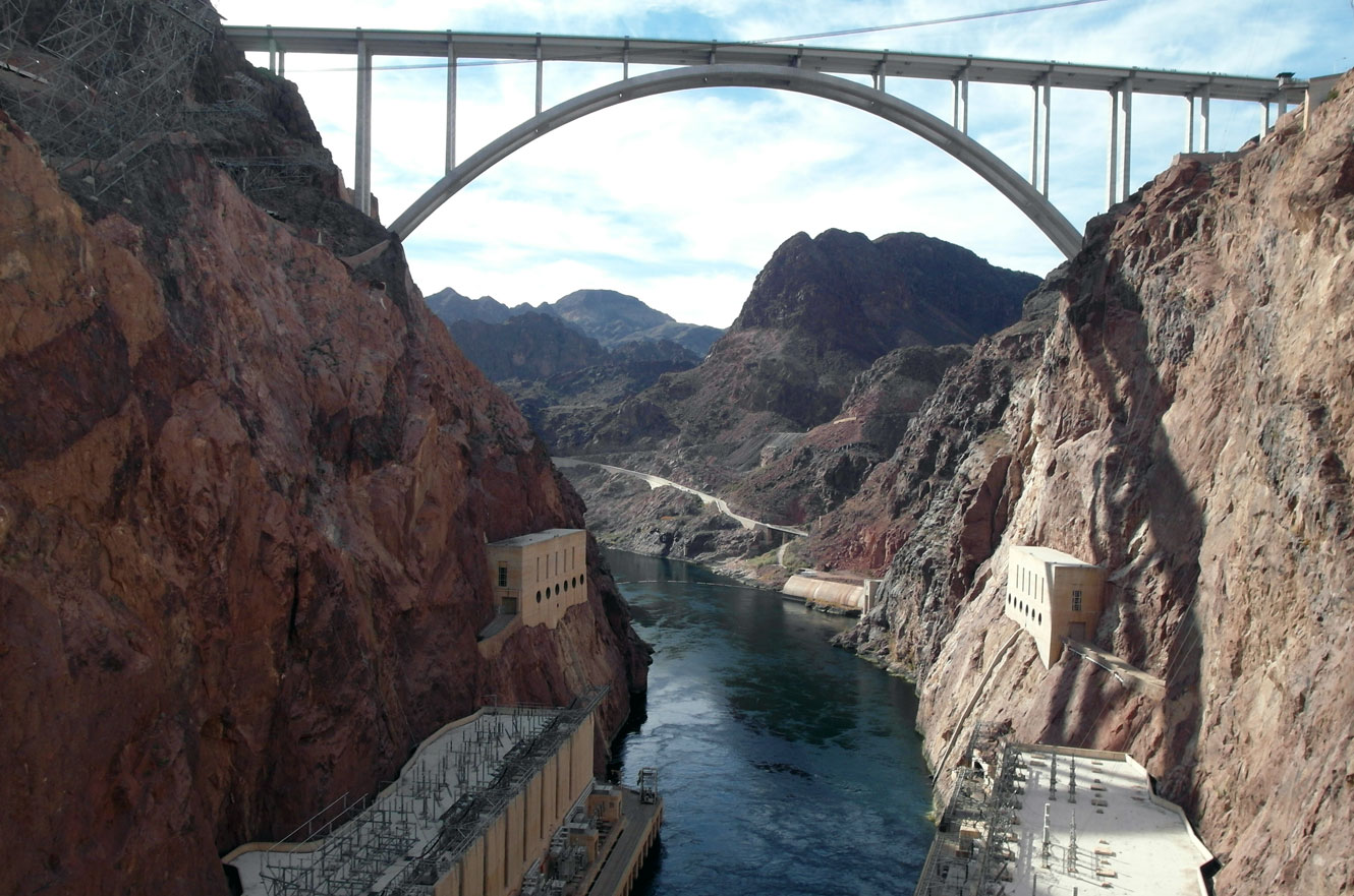 The Mike O'Callaghan-Pat Tillman Memorial Bridge arching over the Colorado River canyon downstream of Hoover Dam, with the powerhouses visible on either bank