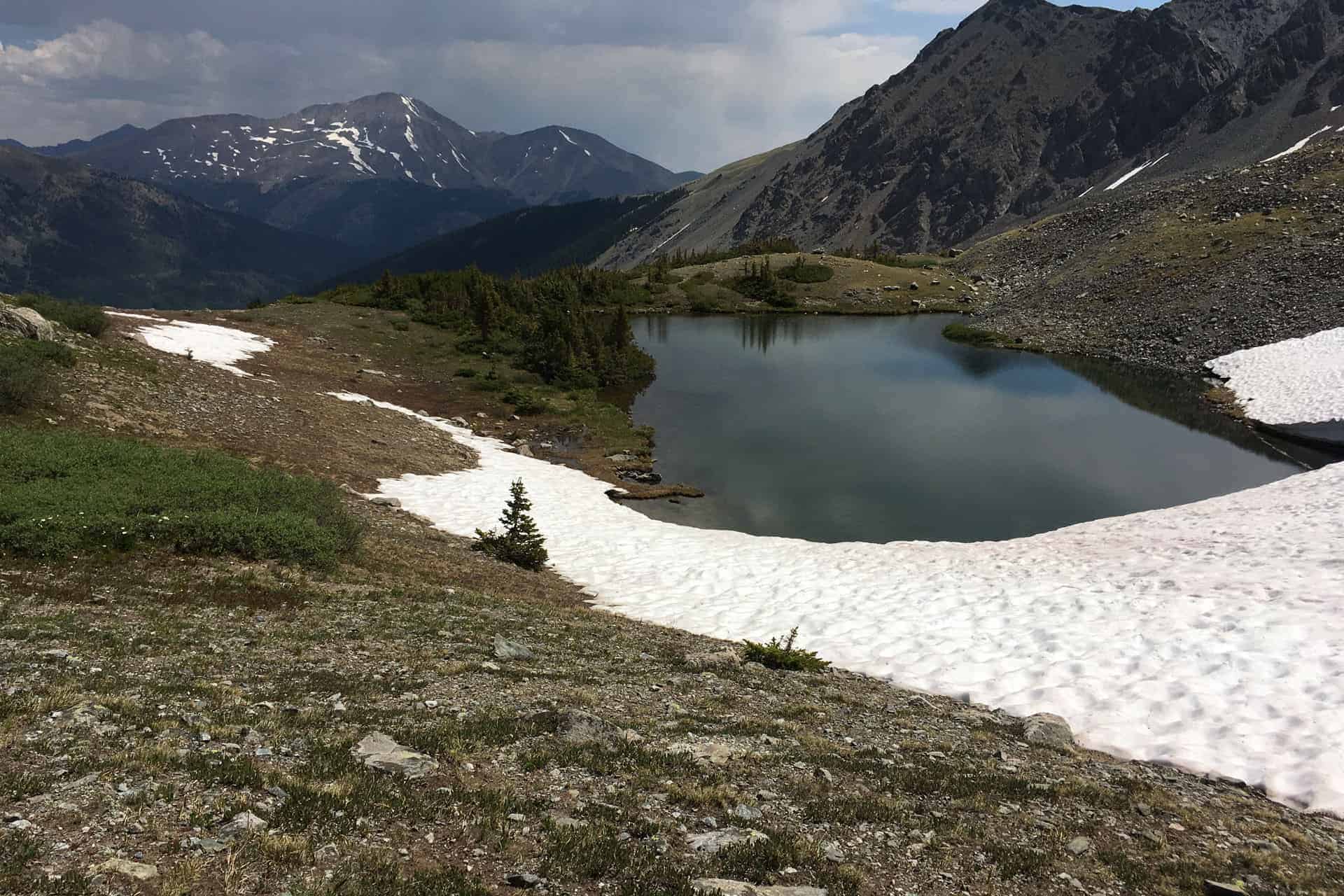 A dirt trail winding across a grassy alpine plateau toward distant mountains under a blue sky