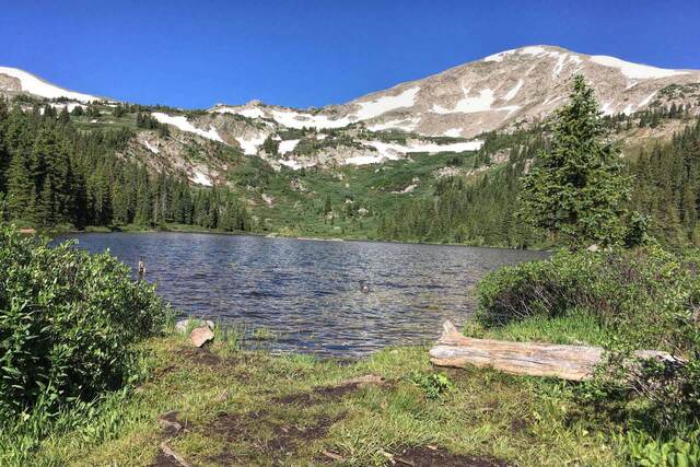 Kroenke Lake reflecting a snow-streaked mountain ridge under a clear blue sky