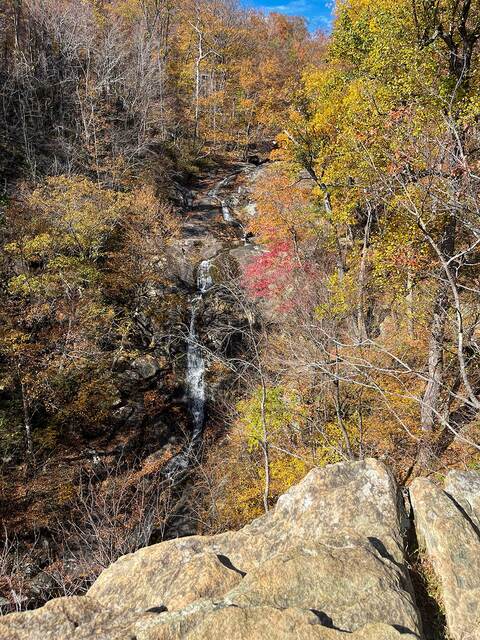 A waterfall seen from a cliffside overlook, surrounded by fall color