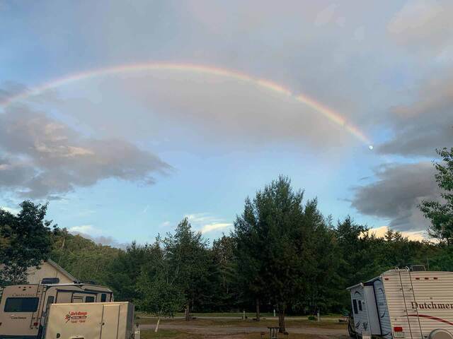 A rainbow arching over the RVs at the campground, with the moon visible at its end
