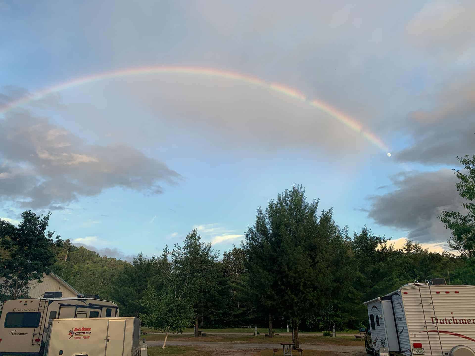 A rainbow arching over the RVs at the campground, with the moon visible at its end