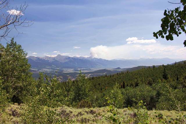 A hazy mountain valley view with a large plume of wildfire smoke rising on the horizon