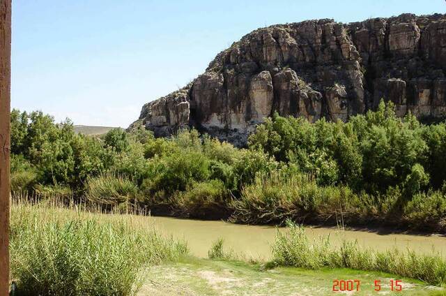 The muddy Rio Grande winding along the base of a sheer rock bluff in Big Bend National Park